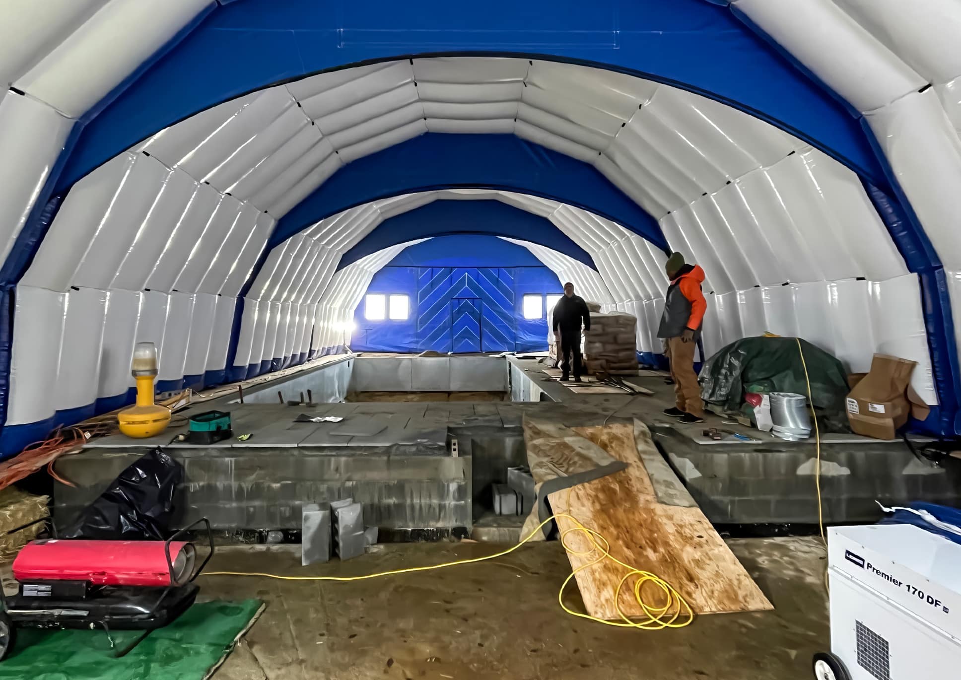 Workers building a swimming pool inside a blue CA-10 Fast Tent